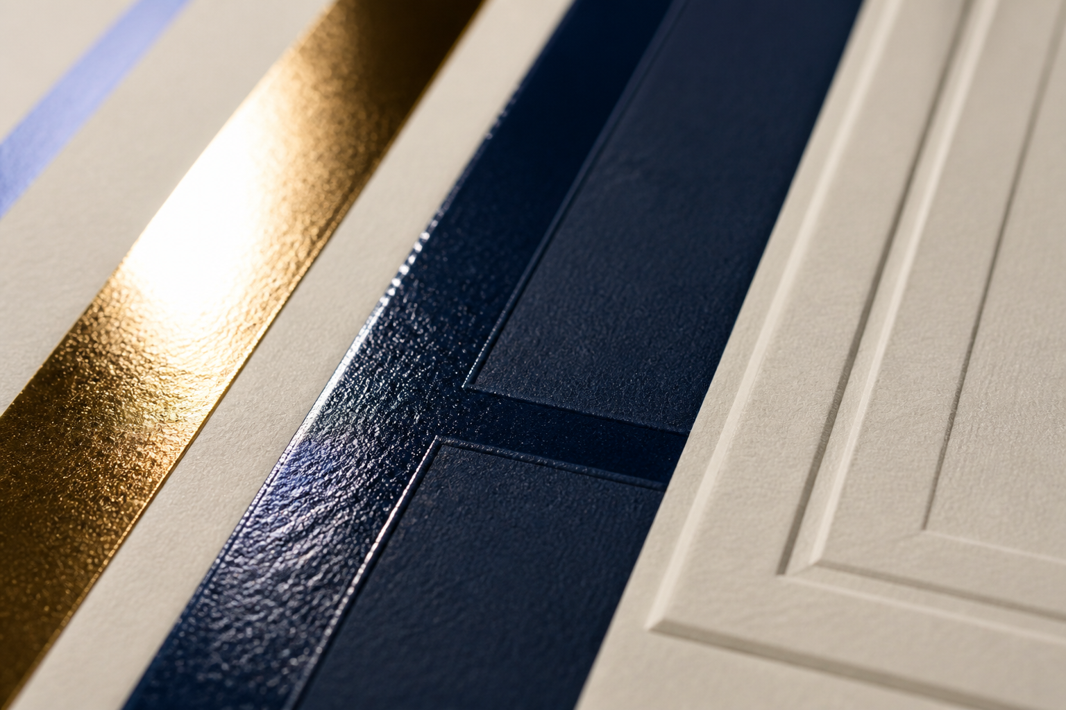 Macro of print finishes — gold foil, navy spot-UV gloss over matte, and a blind emboss on cream stock