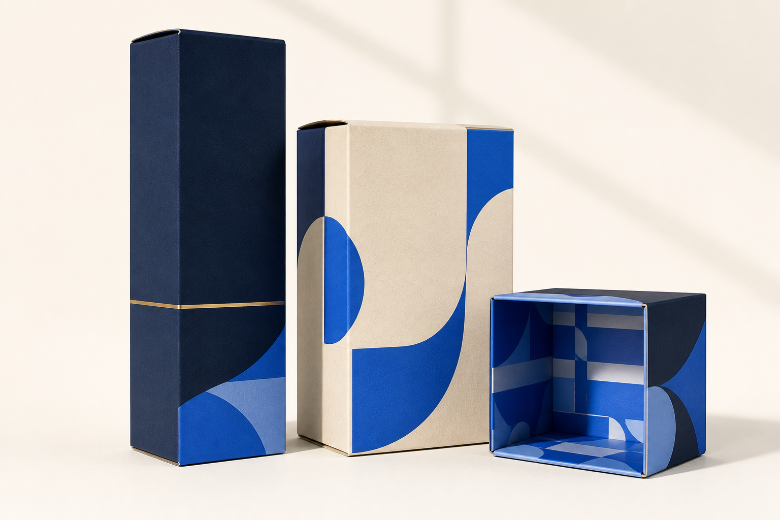 Three folding carton boxes with blue and navy print, one open to show the printed interior, on a cream studio background